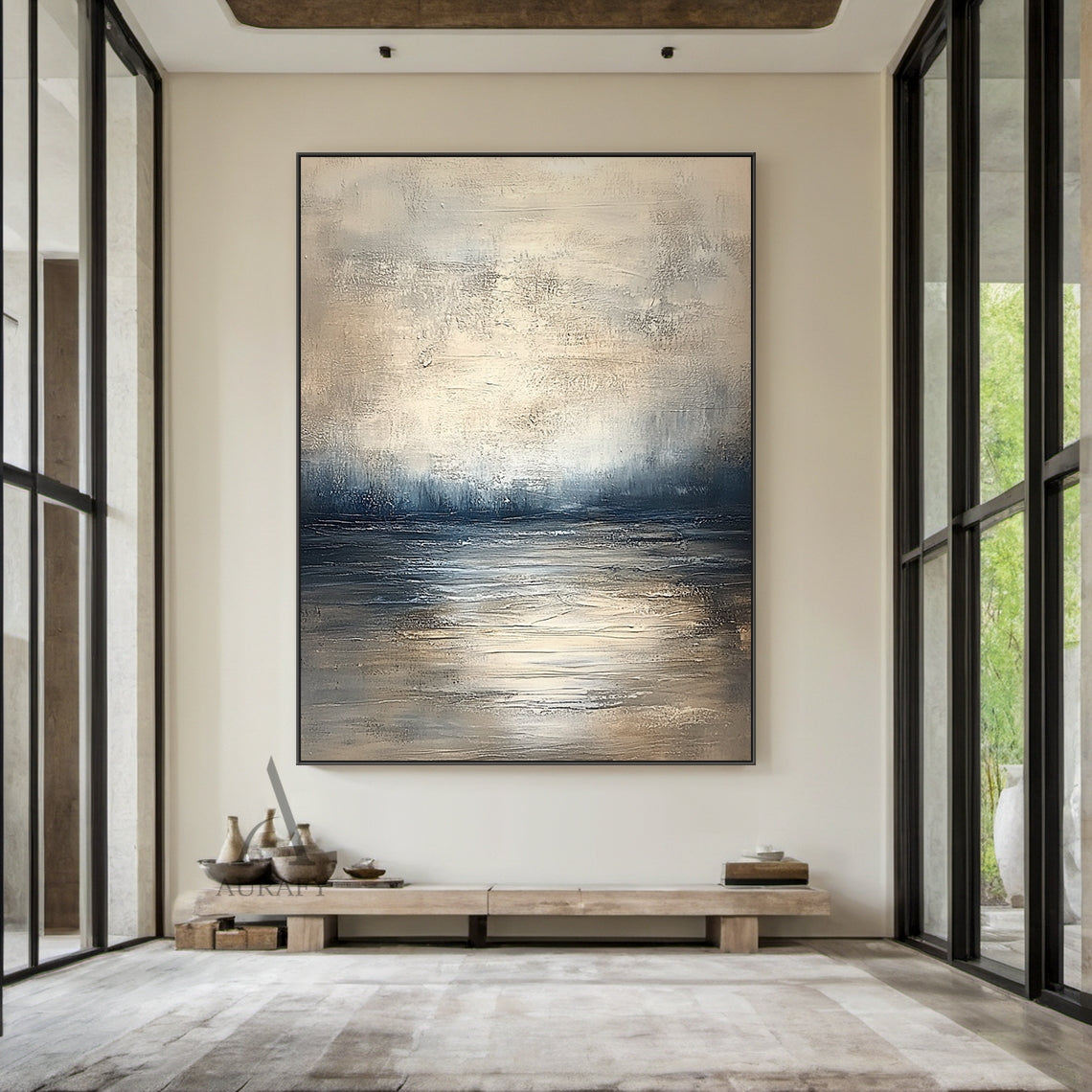 Abstract beige blue wall art (AURA405) real-life decor display shot, retains knife stroke textured surface, horizontal layered composition with soft gradient between light beige, gray beige, deep blue and gray blue tones that evokes calm water surface, distant shoreline and misty hazy sky in sequence. This image shows the artwork matched with natural wood frame hung above a beige linen sofa as living room background decor, the handcrafted thick paint texture delivers serene tranquil natural vibe, perfectly