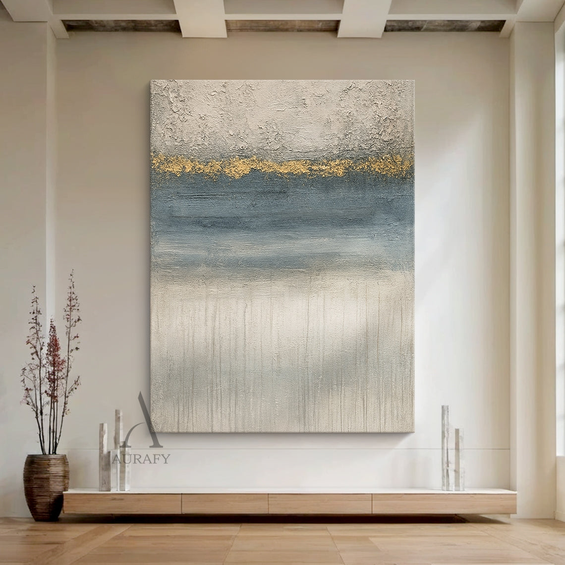 General abstract gray blue plaster textured wall art (AURA405) shown in styled modern home scene, with its iconic horizontal layered composition: top rough thick impasto light gray plaster texture, middle irregular textured gold accent band as visual focal point, followed by gradient blue section with horizontal brushstrokes, bottom light gray layer with vertical dripping texture. This modern organic wabi-sabi style artwork blends perfectly with surrounding neutral home furnishings, ideal for Japandi, minim