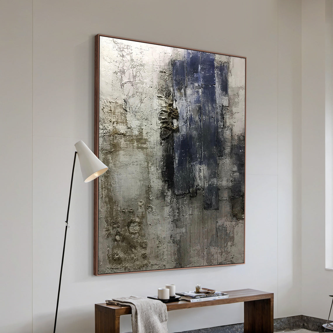 AURA223 Wabi Sabi Abstract Wall Art featuring layered impasto strokes and cracked textures in brown, black, deep blue, and neutral tones. Displayed in a sunlit living room setting with a light wood sofa adorned with soft neutral throw pillows, a woven jute rug underfoot, natural light filtering through sheer white curtains, a small round side table holding a ceramic vase of dried pampas grass, and a minimalist floor lamp casting warm glow—perfect for living room, bedroom, or office decor. Embodies the Wabi