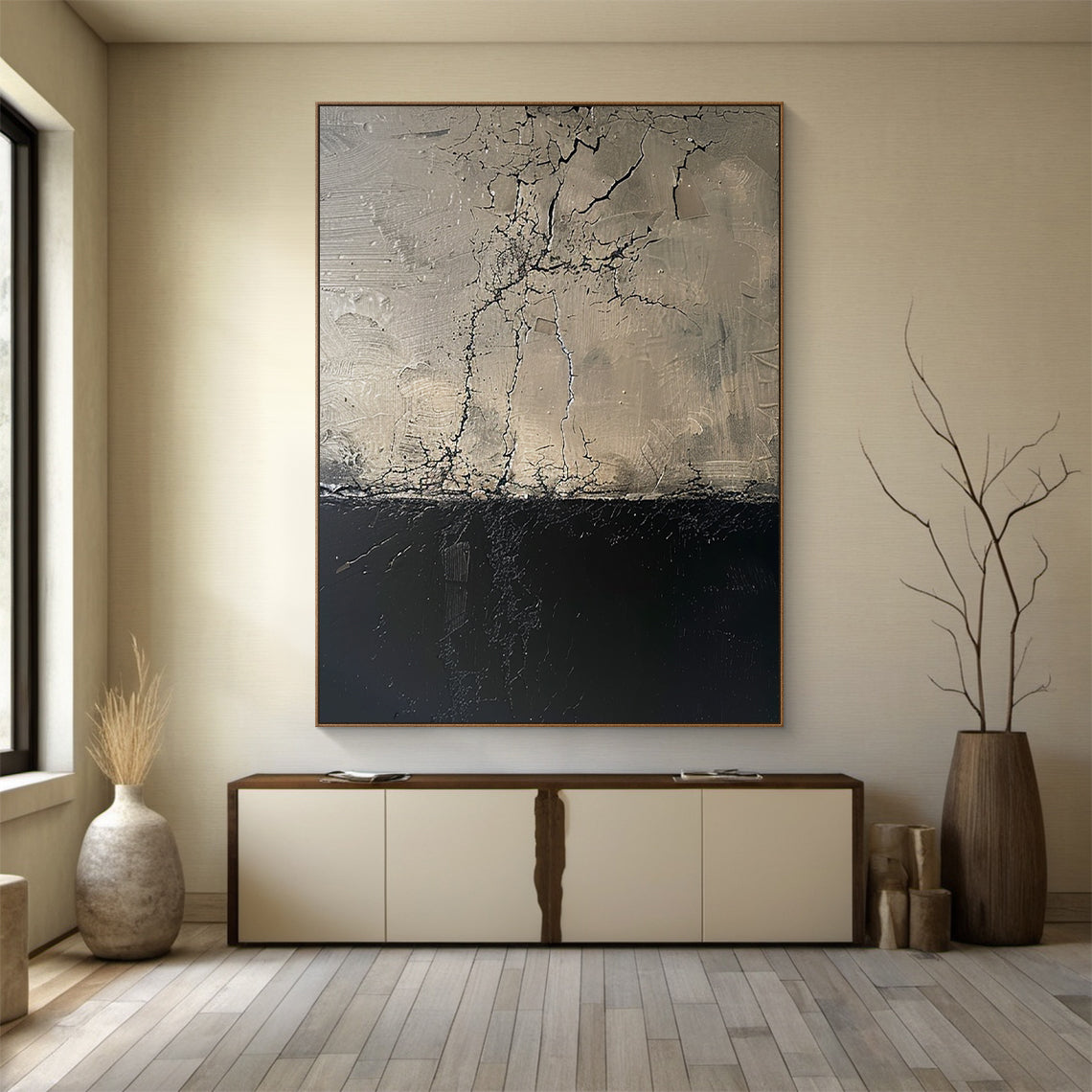 Vertical abstract painting with upper beige-gray section (crack-like linear patterns, impasto texture) and lower deep black section, framed in thin warm brown. Hung above modern light beige console table with dark brown accents in a minimalist room: soft beige walls, light gray wood plank flooring, light beige ceramic vase (dried grass) and dark brown wooden vase (bare branches) nearby. This piece serves as a focal point in the serene, sophisticated space.