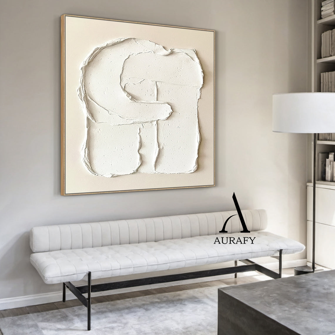 Aurafy AURA541 minimalist plaster textured wall art, warm soft beige canvas base with hand-applied thick impasto matte white 3D abstract capital letter G shape, with irregular handcrafted rough edges, natural porous surface details and texture folds, real shot hung on off-white matte living room accent wall, with light gray linen sofa and small teak side table in the background, neutral tone wabi sabi japandi wall decor for modern minimalist, Scandinavian and cozy neutral home.