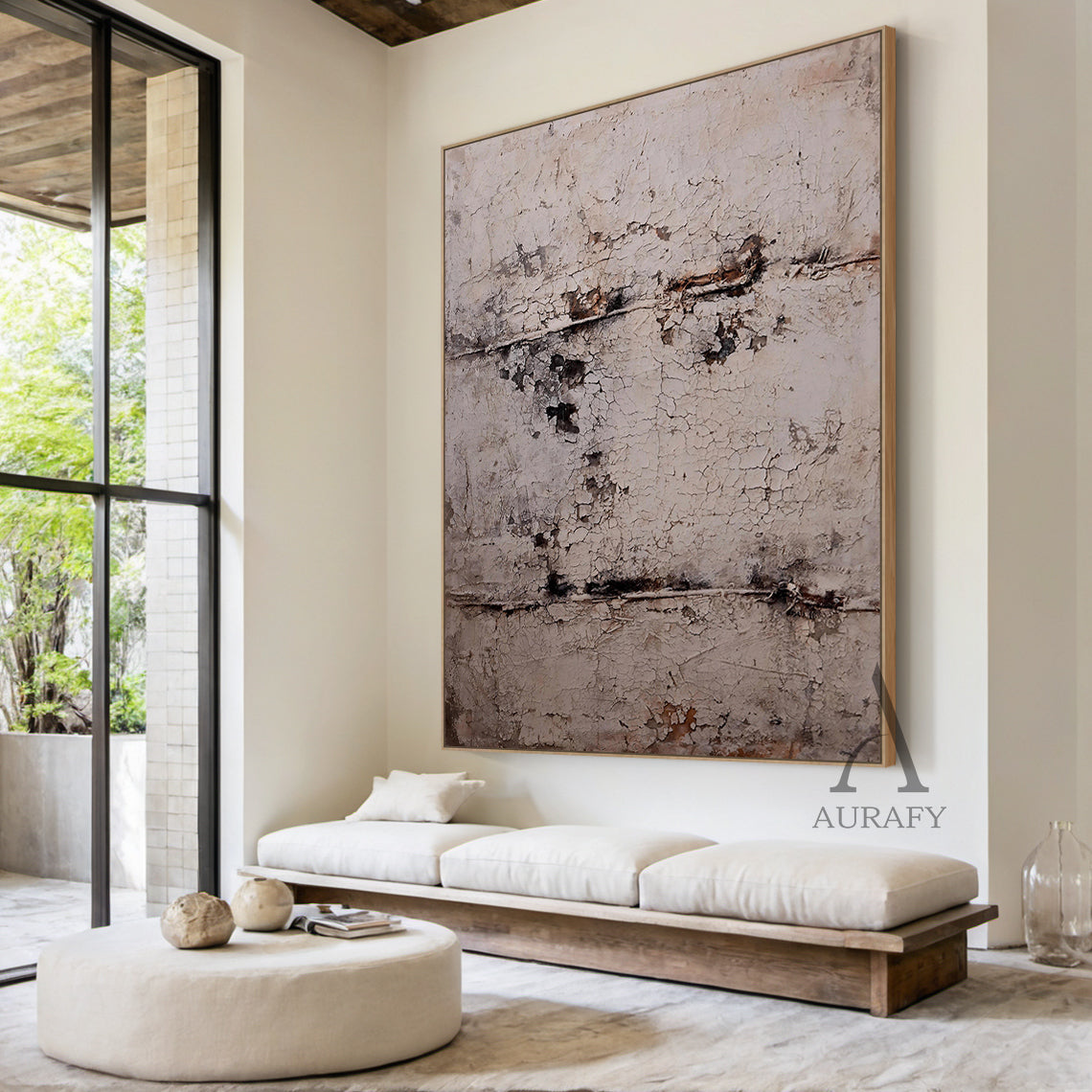Large vertical abstract wall art with a textured, cracked surface in neutral beige, gray, and subtle brown/black tones, framed in a thin brown border. Displayed in a sleek modern living room setting above a low-profile linen sofa, adjacent to a minimalist black metal floor lamp and a small marble decorative tray holding a citrus-scented candle—ideal for infusing contemporary living spaces with understated artistic charm.