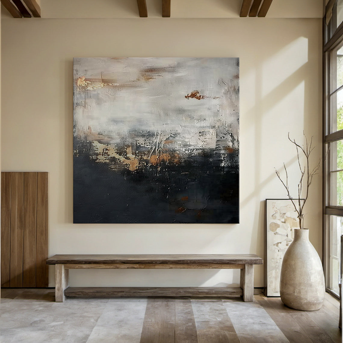 Wabi Sabi abstract sculpted canvas art with impasto knife strokes and tactile surface—deep black lower section, light gray upper layer, golden copper accents. Displayed in a serene modern organic space: light beige walls, wooden ceiling, soft-cushioned bench, gray rug, metallic vase with branches, natural light. Embraces Wabi Sabi’s imperfect beauty and subtle warm softness (Pink vibe) for calm, minimalist home decor. AURA196.