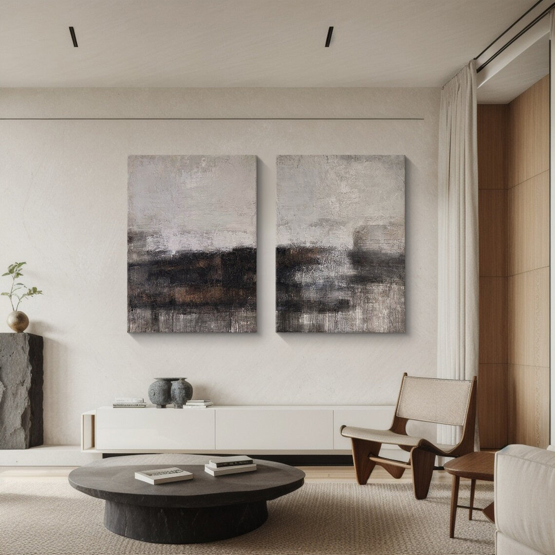 Two-piece Wabi Sabi abstract art set leaning against a white minimalist TV stand in a warm inviting living room. Each canvas features tactile knife strokes, warm neutral tones (soft beige, deep charcoal, earthy brown) with subtle pink undertones, and intentional imperfect textures. The space includes a woven jute rug, a ceramic vase with dried pampas grass, and a soft floor lamp—ideal for creating a cozy, calm living area with natural-inspired charm.