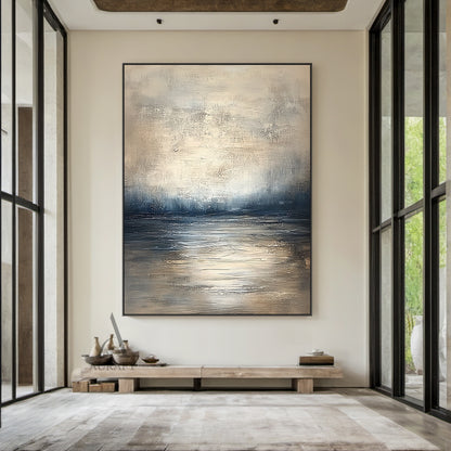 Abstract beige blue wall art (AURA405) real-life decor display shot, retains knife stroke textured surface, horizontal layered composition with soft gradient between light beige, gray beige, deep blue and gray blue tones that evokes calm water surface, distant shoreline and misty hazy sky in sequence. This image shows the artwork matched with natural wood frame hung above a beige linen sofa as living room background decor, the handcrafted thick paint texture delivers serene tranquil natural vibe, perfectly 