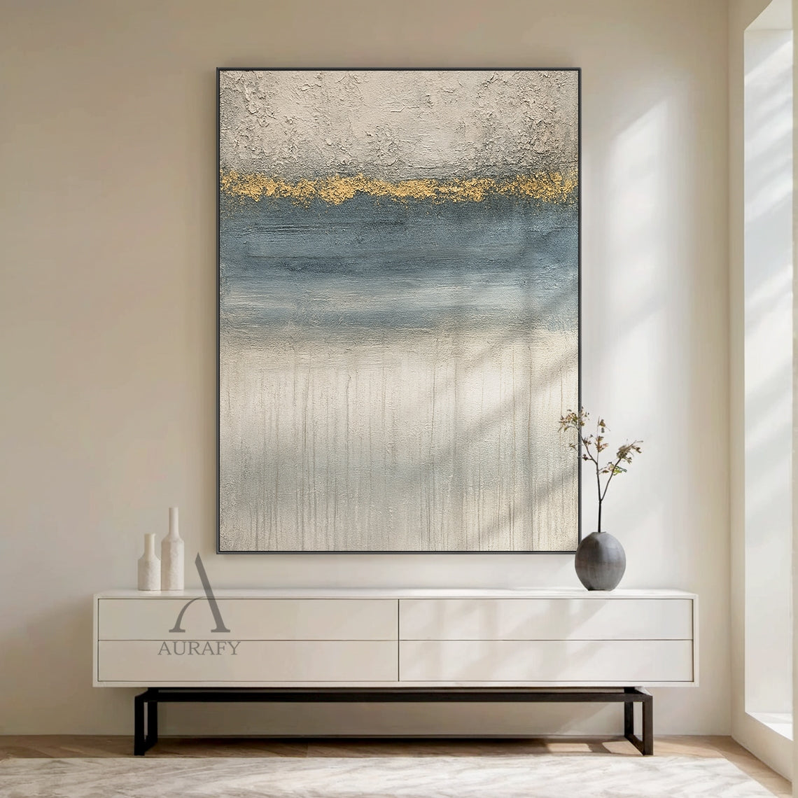 General abstract gray blue plaster textured wall art (AURA405) shown in warm minimalist home display scene, with its iconic horizontal layered composition: top rough thick impasto light gray plaster texture, middle irregular textured gold accent band as visual focal point, followed by gradient blue section with horizontal brushstrokes, bottom light gray layer with vertical dripping texture. This modern organic wabi-sabi style artwork blends perfectly with surrounding warm textured soft home furnishings, ide