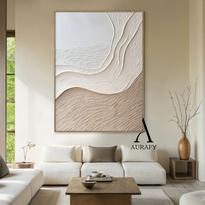 Aurafy AURA539 minimalist beige wall art, plaster textured high relief abstract canvas artwork. Displays the piece hung above a low oak sideboard against a soft white wall, its monochromatic soft gradient from cool off-white to warm light khaki beige blends seamlessly with neutral linen and jute decor accents, the organic undulating flowing curves inspired by wind-swept sand dunes and gentle shore slopes cast subtle soft shadows under ambient light, highlighting the raised impasto surface with fine linear s