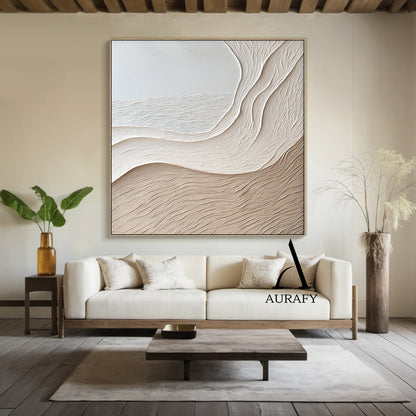 Aurafy AURA539 minimalist beige wall art, plaster textured high relief abstract canvas artwork. Displays the piece hung above a low oak sideboard against a soft white wall, its monochromatic soft gradient from cool off-white to warm light khaki beige blends seamlessly with neutral linen and jute decor accents, the organic undulating flowing curves inspired by wind-swept sand dunes and gentle shore slopes cast subtle soft shadows under ambient light, highlighting the raised impasto surface with fine linear s