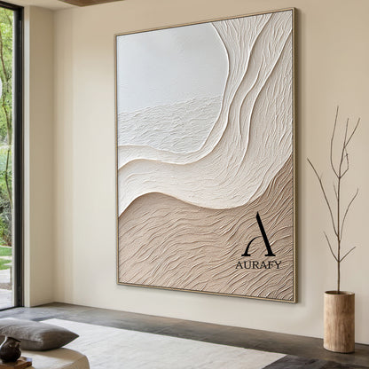 Aurafy AURA539 minimalist beige wall art, plaster textured high relief abstract canvas artwork. Displays the piece hung above a cream fabric sofa against a soft milk tea colored accent wall, its monochromatic soft gradient from cool off-white to warm light khaki beige blends seamlessly with fuzzy knit throw, natural rattan floor lamp and light oak coffee table decor accents, the organic undulating flowing curves inspired by wind-swept sand dunes and gentle shore slopes cast subtle soft shadows under warm re