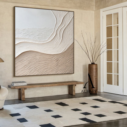 Aurafy AURA539 minimalist beige wall art, plaster textured high relief abstract canvas artwork. Displays the piece hung above a cream fabric sofa against a soft milk tea colored accent wall, its monochromatic soft gradient from cool off-white to warm light khaki beige blends seamlessly with fuzzy knit throw, natural rattan floor lamp and light oak coffee table decor accents, the organic undulating flowing curves inspired by wind-swept sand dunes and gentle shore slopes cast subtle soft shadows under warm re