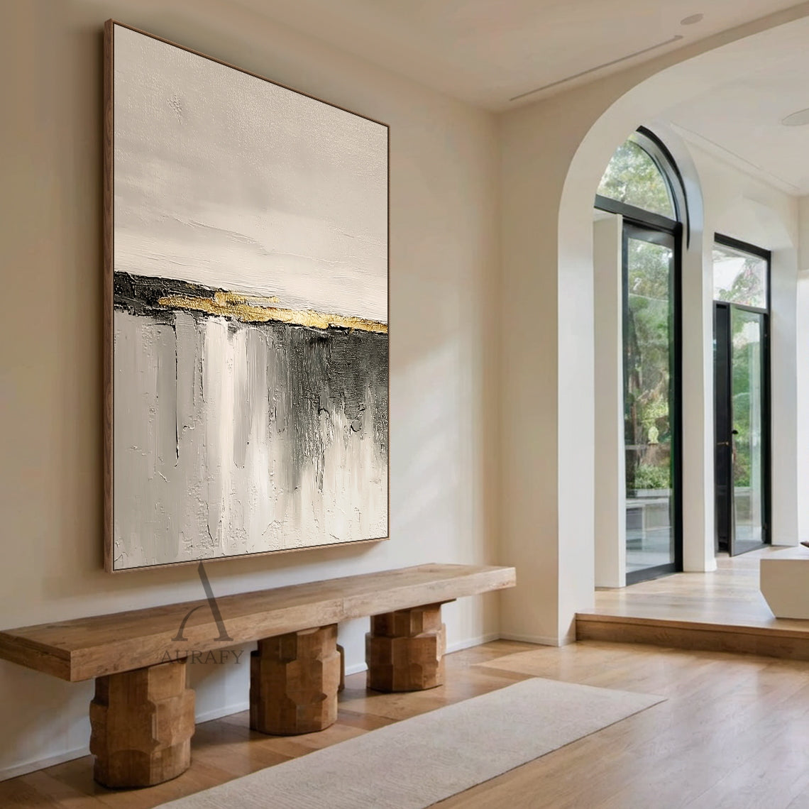 Hand-painted beige abstract impasto canvas wall art AURA718, displayed hanging on a matte warm white living room wall above a light oak low sideboard in a real neutral home styling scene, the artwork features soft warm off-white and light beige with subtle thick paint grain texture on the upper section, central horizontal matte charcoal stripe accented with raised grainy metallic gold thick paint band as focal point, lower area is gradient gray from light beige gray to dark charcoal with vertical sweeping b