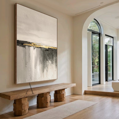 Hand-painted beige abstract impasto canvas wall art AURA718, displayed hanging on a matte warm white living room wall above a light oak low sideboard in a real neutral home styling scene, the artwork features soft warm off-white and light beige with subtle thick paint grain texture on the upper section, central horizontal matte charcoal stripe accented with raised grainy metallic gold thick paint band as focal point, lower area is gradient gray from light beige gray to dark charcoal with vertical sweeping b