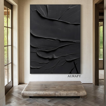 Black minimalist textured abstract wall art, featuring thick impasto knife-scraped matte black paint strokes with natural flowing undulations, raised ridges and subtle brush marks. All light and shadow variations come from the dimensional texture's light reflection difference, no extra pigments are added, with a tiny AURAFY brand logo at the bottom right corner, suitable for wabi-sabi, Japandi, modern industrial interior decor.
