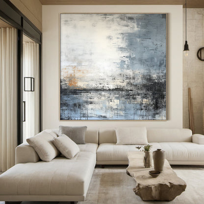 Modern abstract blue geometric wall art with textured brushwork: shades of gray-blue, cobalt, white, gray, black, and subtle warm orange accents. Features abstract blocks and thick impasto texture. Displayed above a beige fabric bed in a Nordic-style bedroom—perfect focal point for minimalist, Nordic, or modern home decor. Ready-to-hang with a sleek black aluminum frame and premium waterproof canvas.