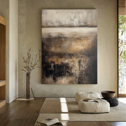 Horizontal earthy brown abstract textured painting SKU AURA617 in real japandi home styling scene: the wabi-sabi minimalist organic artwork is mounted on light beige textured wall above a low solid wood sideboard, matched with woven rattan ornament and dried reed arrangement placed on the cabinet top, the painting's layered structure is clearly presented under soft diffused natural light -- upper hazy section blending light off-white and pale beige, lower part with overlapping rich dark brown, charcoal blac