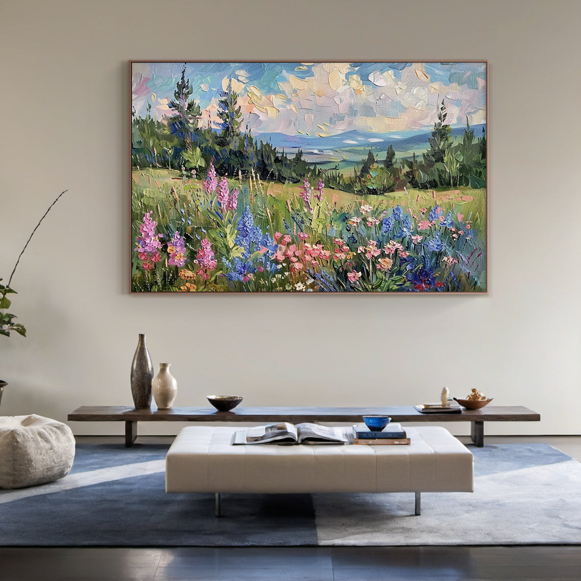 Impasto palette knife impressionism oil painting, alpine mountain landscape artwork. Foreground has vibrant wildflower meadow with pink lupines, blue delphiniums, peach, butter yellow, red small wild blooms and green grasses. Middle ground features dense evergreen coniferous forest slopes and rolling grass valleys. Background is hazy layered blue-grey mountains, light blue sky with warm golden and blush tinted sunset clouds. Thick textured block brushstrokes, modern nature wall art for home decor.