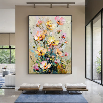 Impasto palette knife oil painting of wild clustered florals, presented in a real modern organic home styling scene. The artwork features fully bloomed, half-opened and budding flowers in soft buttery yellow, blush pink, light peach shades, paired with muted sage green stems and foliage against a neutral creamy beige textured background. Thick raised paint strokes create a distinct tactile hand-painted texture, following the impressionist wabi-sabi decorative style, which matches perfectly with light wood f
