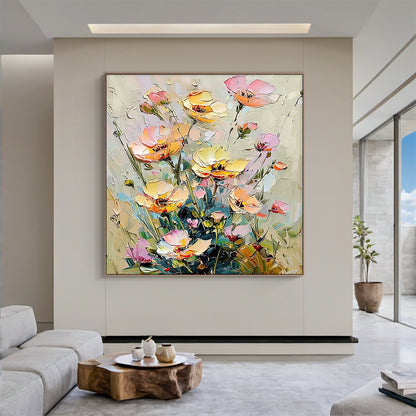 Impasto palette knife oil painting of wild clustered florals, presented in a real modern organic home styling scene. The artwork features fully bloomed, half-opened and budding flowers in soft buttery yellow, blush pink, light peach shades, paired with muted sage green stems and foliage against a neutral creamy beige textured background. Thick raised paint strokes create a distinct tactile hand-painted texture, following the impressionist wabi-sabi decorative style, which matches perfectly with light wood f