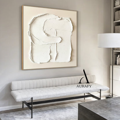 Aurafy AURA541 minimalist plaster textured wall art, warm soft beige canvas base with hand-applied thick impasto matte white 3D abstract capital letter G shape, with irregular handcrafted rough edges, natural porous surface details and texture folds, real shot hung on off-white matte living room accent wall, with light gray linen sofa and small teak side table in the background, neutral tone wabi sabi japandi wall decor for modern minimalist, Scandinavian and cozy neutral home.