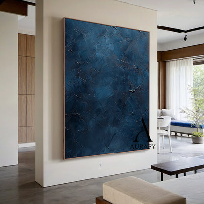 Handcrafted navy blue abstract minimalist canvas wall art staged living room wall display, showcasing a thick hand-applied impasto palette knife textured surface with irregular raised scrapes, subtle embedded metallic shimmer flecks, layered muted blue hues ranging from soft slate blue to deep midnight navy, no figurative patterns, this wabi-sabi Japandi style artwork from Aurafy is ideal for modern minimalist, wabi-sabi and Japandi interior wall decor.