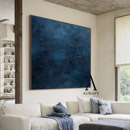 Handcrafted navy blue abstract minimalist canvas wall art staged living room wall display, showcasing a thick hand-applied impasto palette knife textured surface with irregular raised scrapes, subtle embedded metallic shimmer flecks, layered muted blue hues ranging from soft slate blue to deep midnight navy, no figurative patterns, this wabi-sabi Japandi style artwork from Aurafy is ideal for modern minimalist, wabi-sabi and Japandi interior wall decor.