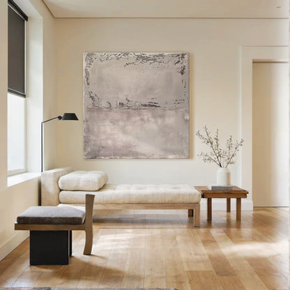 Wabi Sabi Abstract Tactile Impasto Gray Wall Art with Muted Pink Undertones & Distressed Surface (AURA191) - A serene focal point in a bright modern living room. Features layered impasto texture, weathered patterns, soft silvery grays to deep charcoal, subtle pink hints. Displayed against neutral walls, complementing natural light, wooden console, white sofa, and large windows with greenery views. Ideal for minimalist, organic home decor.