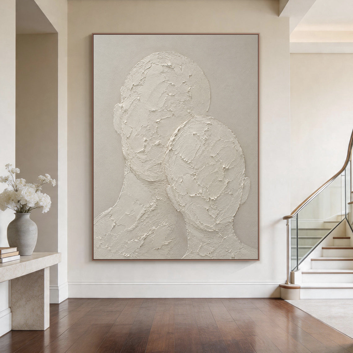 Wabi-sabi beige 3D textured plaster canvas wall art hung above the low-profile light oak headboard of a soothing Japandi primary bedroom, handcrafted with thick impasto knife strokes, displays two faceless abstract head and neck silhouettes in an intimate leaning snuggling pose. It has raised, cracked, rough tactile texture against a smooth muted warm beige background, with a monochromatic neutral off-white soft taupe palette, this minimalist Japandi figurative artwork perfectly complements warm, textural h