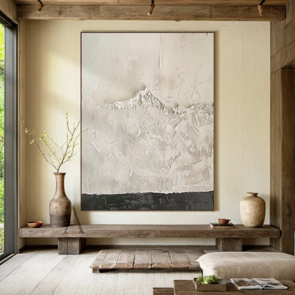 Beige wabi-sabi abstract textured canvas wall art, handcrafted with heavy impasto knife painting technique. The artwork is dominated by soft warm off-white and light beige tones, with smooth scraped impasto texture on the upper section, rough granular mountain-like raised texture in the middle that faintly reveals canvas grid, and a narrow deep charcoal textured band at the bottom to balance the visual weight. It is a minimalist Japandi style abstract piece suitable for neutral home interior decoration.