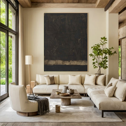 Wabi Sabi Black Abstract Cracked Textured Japandi Canvas Wall Art AURA796 (Scene Display Edition): Minimalist luxe neutral decor artwork presented in real home styling context, retaining its signature deep inky black heavy impasto main field, natural craquelure cracked texture across the full dark surface, subtle warm ochre and gilded undertones peeking through worn hand-applied brush strokes and paint gaps, a muted sand-toned horizontal anchor band at the base, raw woven canvas texture visible through pain