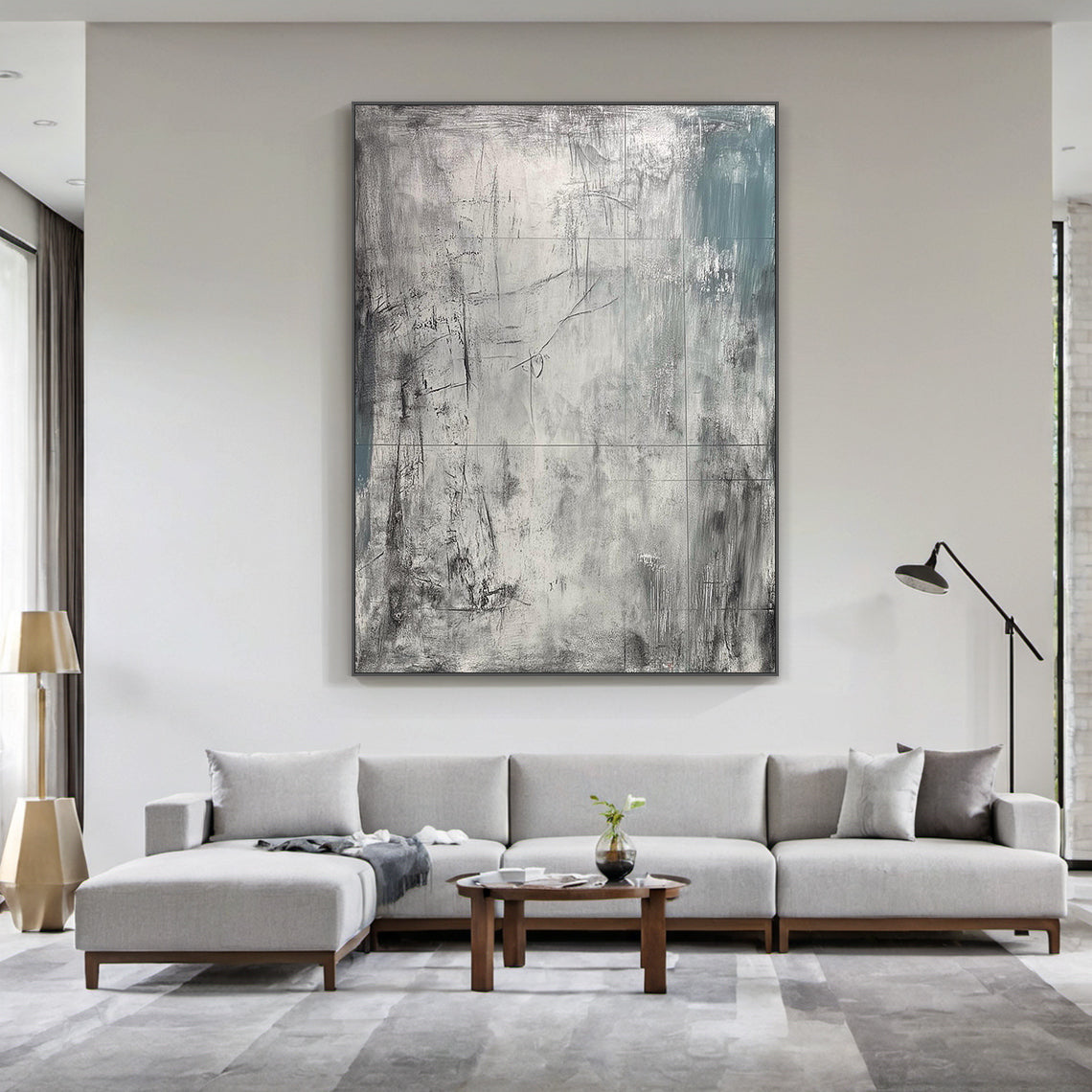 AURA224 Wabi Sabi Gray Abstract Textured Canvas Wall Art - Large statement piece with layered tactile brushstrokes, muted grays, and subtle teal accents, displayed above a gray modular sofa in a modern minimalist living room. Natural light filters through large windows with green outdoor views, complementing neutral Scandinavian-style decor. Ideal focal point for contemporary interiors, enhancing gray wall decor with organic charm.