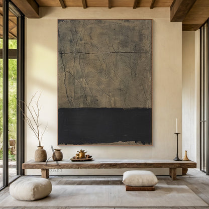 Wabi-sabi minimalist abstract wall art scene display shot, the neutral beige-black Japandi tactile wall decor is hung on the off-white sofa background wall of a modern minimalist living room, the art piece itself features a large warm textured beige upper part with rough grainy weathered finish, dotted with irregular dark thin crack-like lines and a full horizontal dark line running across the entire beige surface, the lower part is a thick matte black horizontal block with natural uneven handcrafted edges,