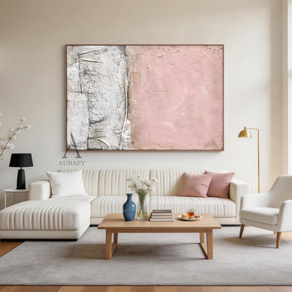 WABI SABI Pink Abstract Textured Wall Art (AURA245) - Soft Blush Upper Half with Visible Brush Strokes & Imperfections, Lower Half in White & Neutral Cracked Layered Finish. Framed in Thin Light Wood Frame. Displayed in Modern Serene Bedroom: Beige Linen Bedding, Light Wood Nightstand with White Ceramic Table Lamp, Small Potted Green Succulent, Warm Yellow Wall Sconce Glow. Perfect for Minimalist Home Decor, Wabi Sabi Inspired Living Space Accent, Cozy Bedroom Wall Decor. AURA245 Collection Merges Wabi Sabi